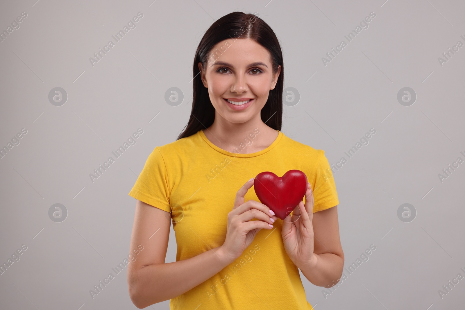 Photo of Happy young woman holding red heart on grey background