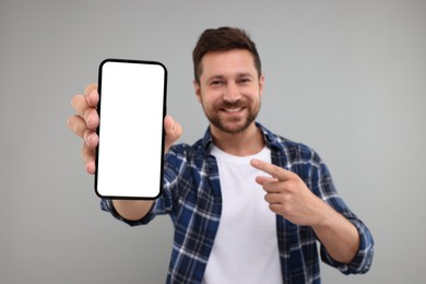 Photo of Handsome man showing smartphone in hand and pointing at it on light grey background, selective focus. Mockup for design
