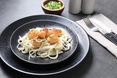 Photo of Delicious scallop pasta with green onion served on grey table