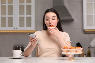 Woman using smartphone while having breakfast at table in kitchen. Internet addiction