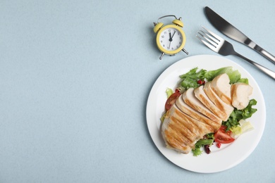 Plate of appetizing food, alarm clock and cutlery on light blue table, flat lay with space for text. Nutrition regime