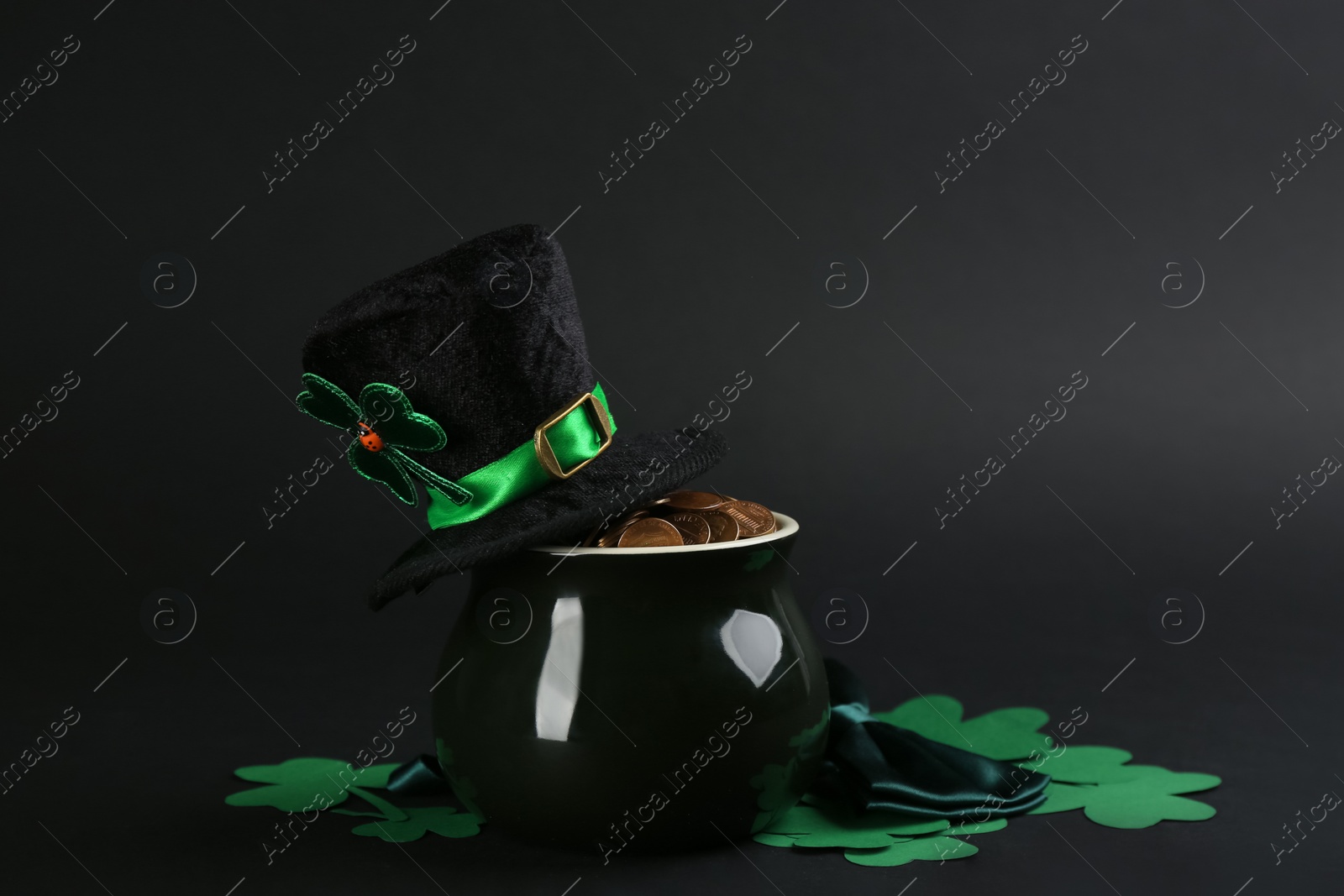 Photo of Composition with pot of gold coins and clover leaves on black background. St. Patrick's Day celebration