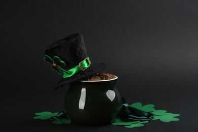 Photo of Composition with pot of gold coins and clover leaves on black background. St. Patrick's Day celebration