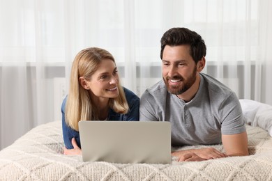 Happy couple with laptop on bed at home