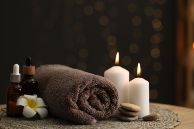 Photo of Spa composition. Rolled towel, cosmetic products, stones, burning candles and plumeria flower on table indoors, closeup. Space for text
