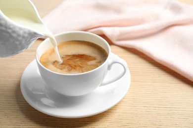 Pouring milk into cup of hot coffee on wooden table