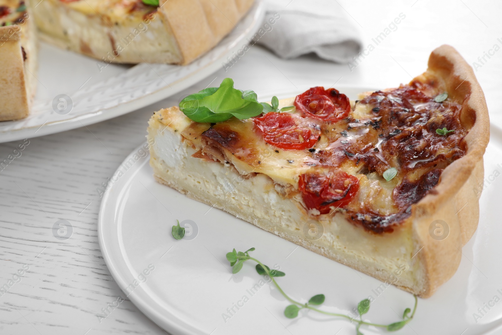 Photo of Piece of delicious homemade quiche with prosciutto and tomatoes on white wooden table, closeup