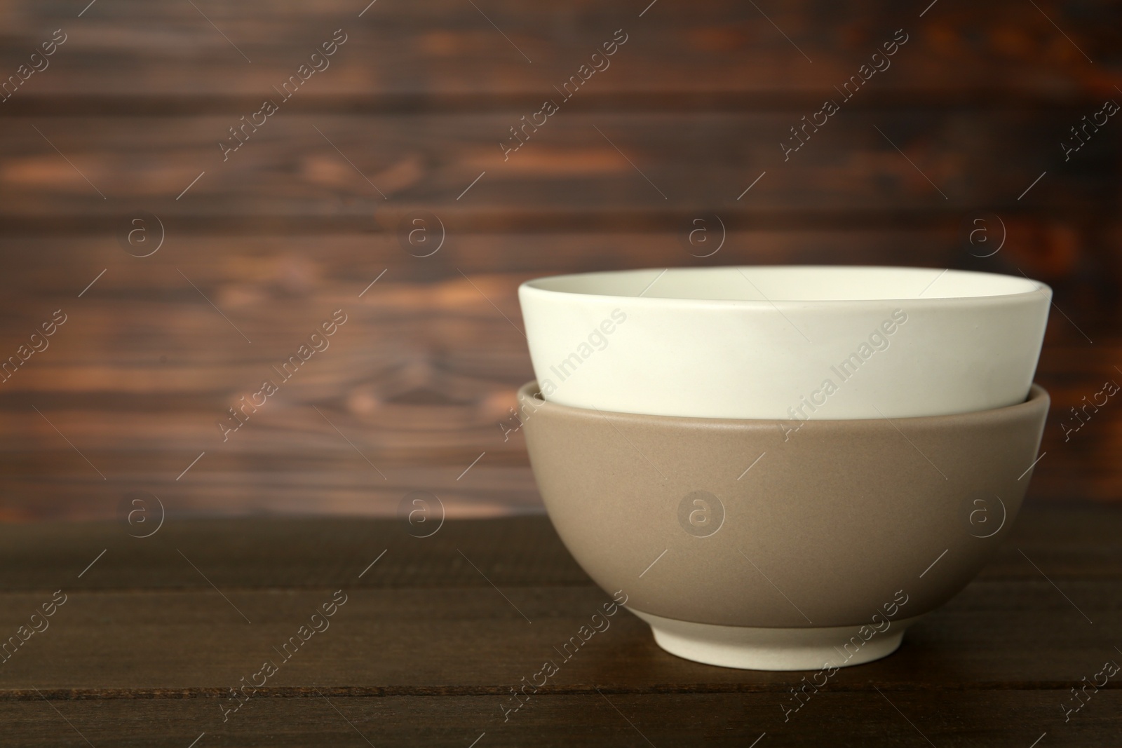 Photo of Stylish empty ceramic bowls on wooden table, space for text. Cooking utensils