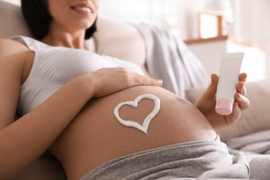 Photo of Young pregnant woman with cosmetic product on sofa indoors, closeup
