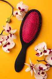 Stylish hairbrush and orchid flowers on yellow background, top view