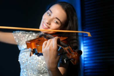 Beautiful young woman playing violin in dark room, focus on hand