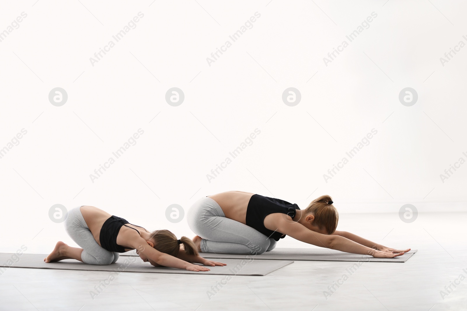 Photo of Mother and daughter in matching sportswear doing yoga together at home