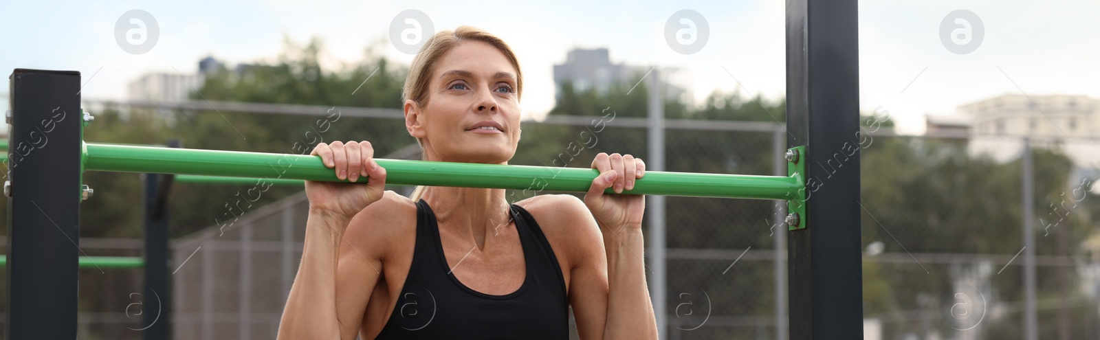 Image of Beautiful woman doing pull-ups at outdoor gym, space for text. Banner design