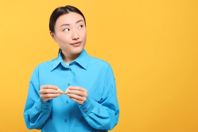 Asian woman breaking tasty fortune cookie with prediction on yellow background, space for text