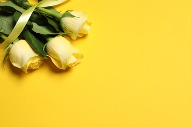 Photo of Beautiful roses and ribbon on yellow background, above view. Space for text