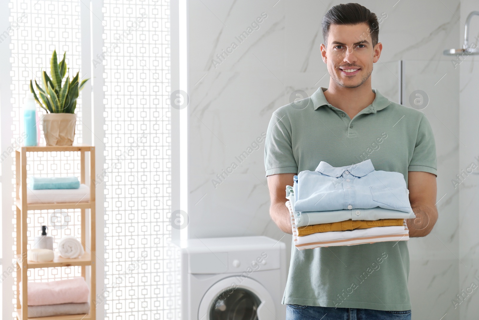 Photo of Happy man with clean clothes in bathroom. Laundry day