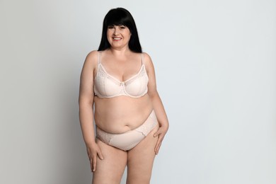 Photo of Beautiful overweight woman in beige underwear on light background, space for text. Plus-size model