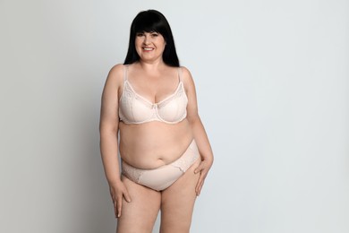 Beautiful overweight woman in beige underwear on light background, space for text. Plus-size model