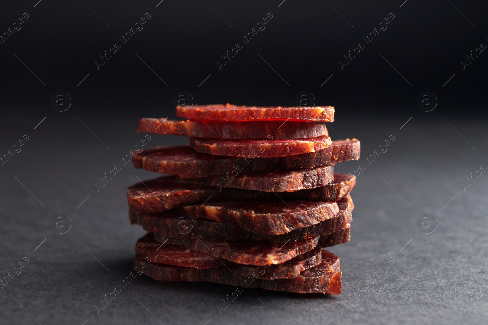 Photo of Stack of delicious beef jerky on dark table, closeup