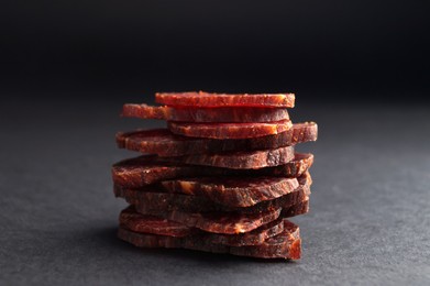 Photo of Stack of delicious beef jerky on dark table, closeup