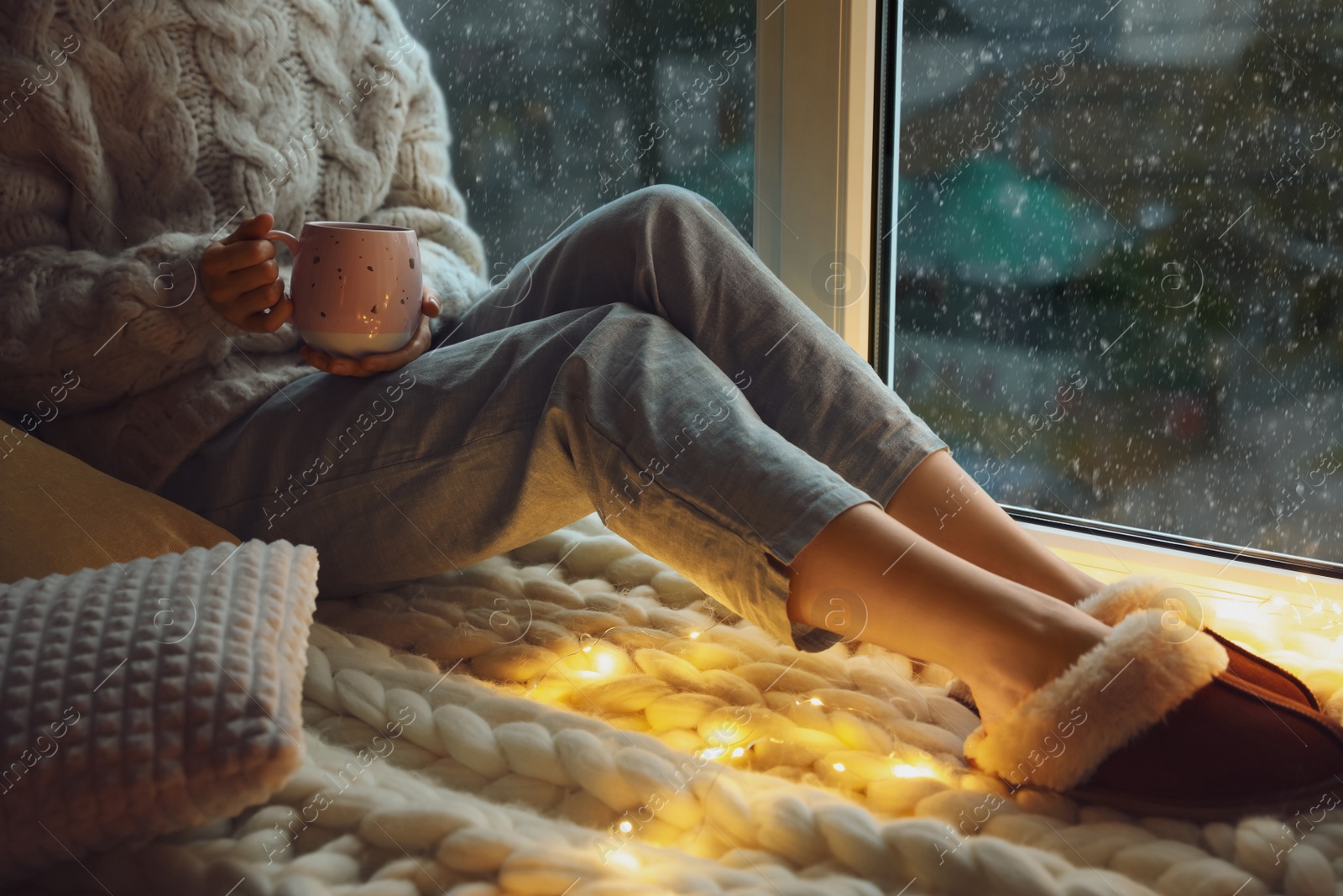 Photo of Woman with drink sitting on soft plaid near window in evening, closeup