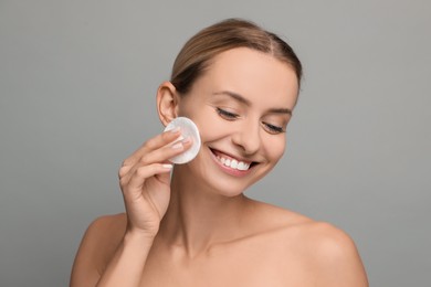 Photo of Smiling woman removing makeup with cotton pad on grey background