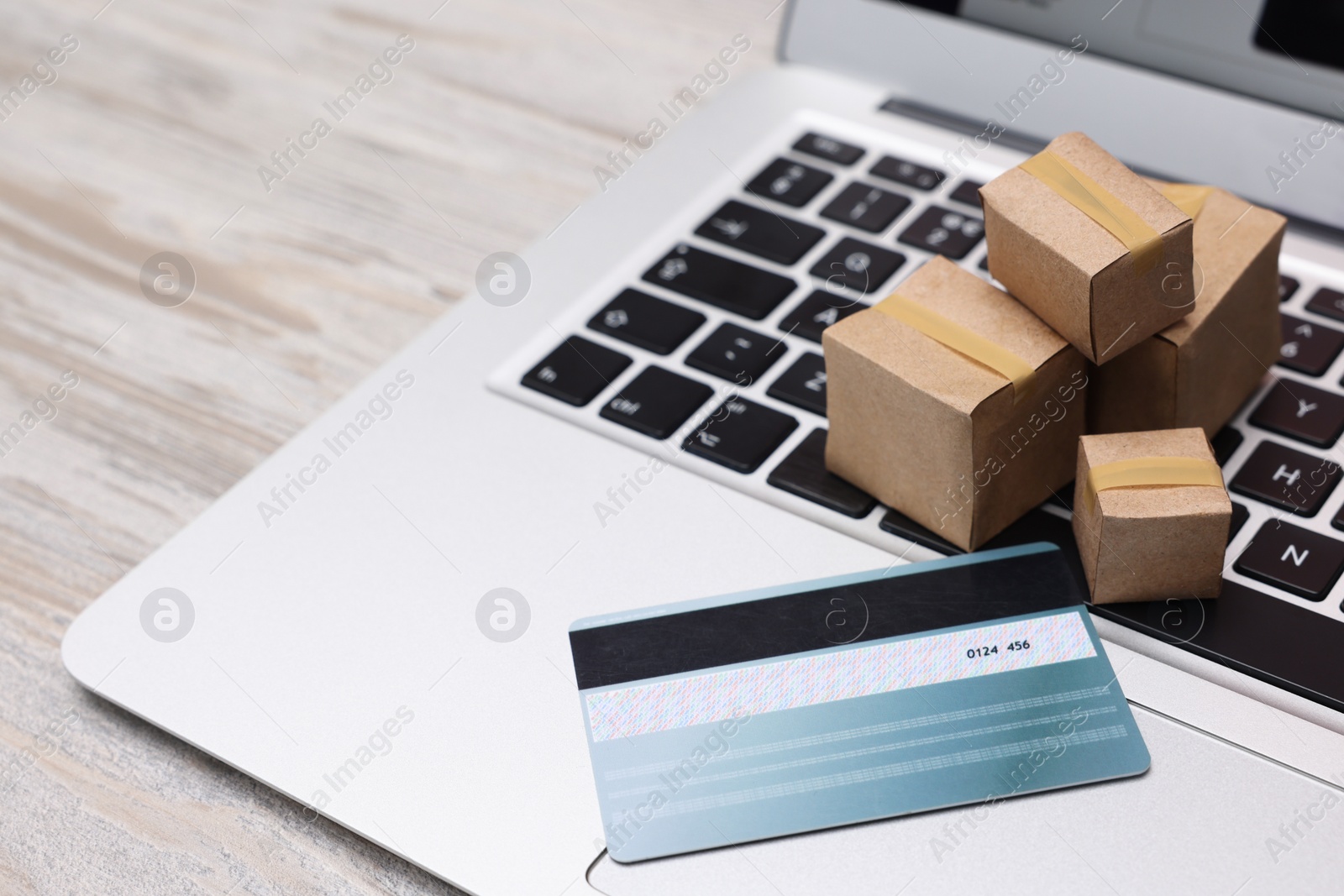 Photo of Internet shopping. Small cardboard boxes, credit card and laptop on light wooden table, closeup. Space for text