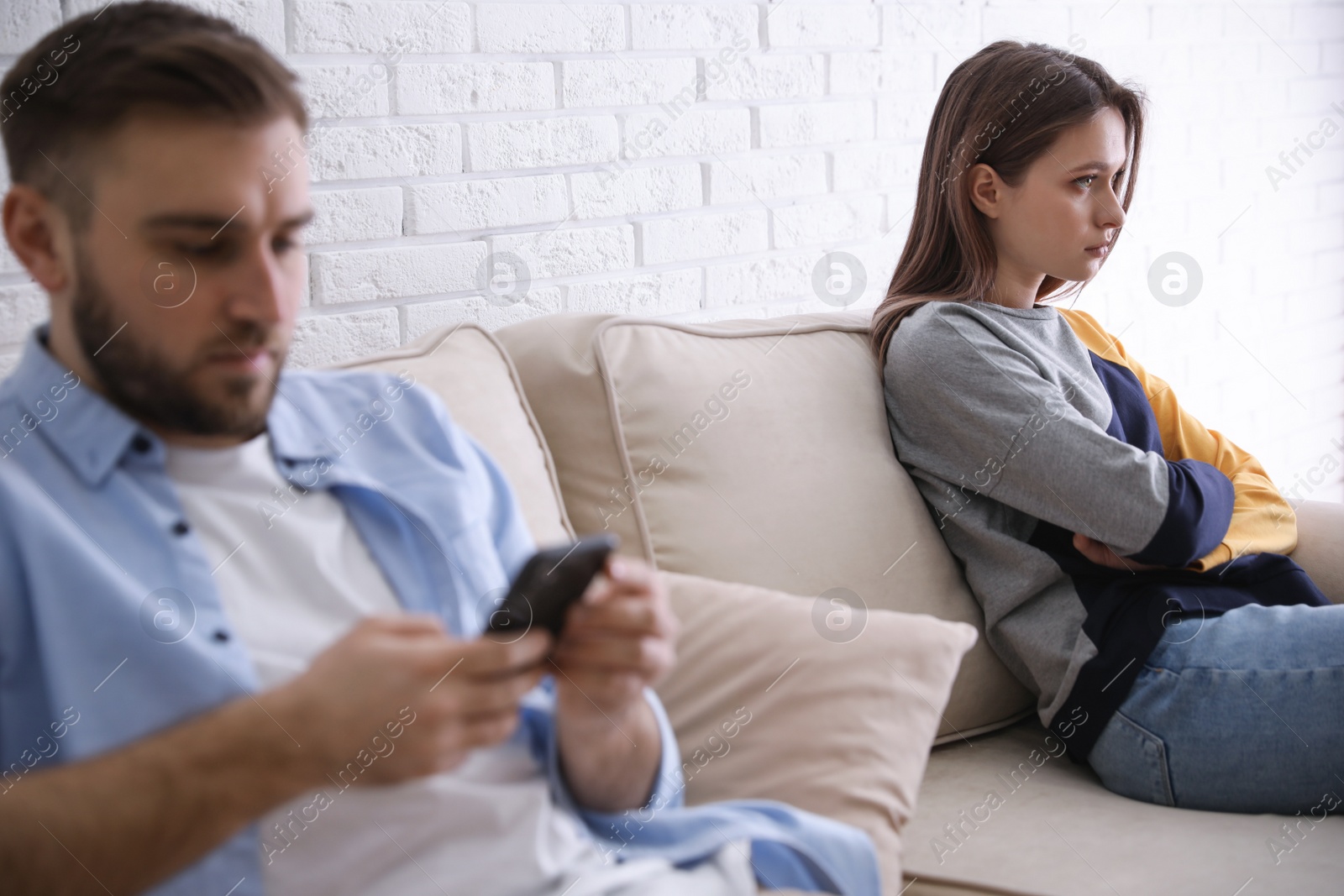 Photo of Young man preferring smartphone over his girlfriend at home. Relationship problems