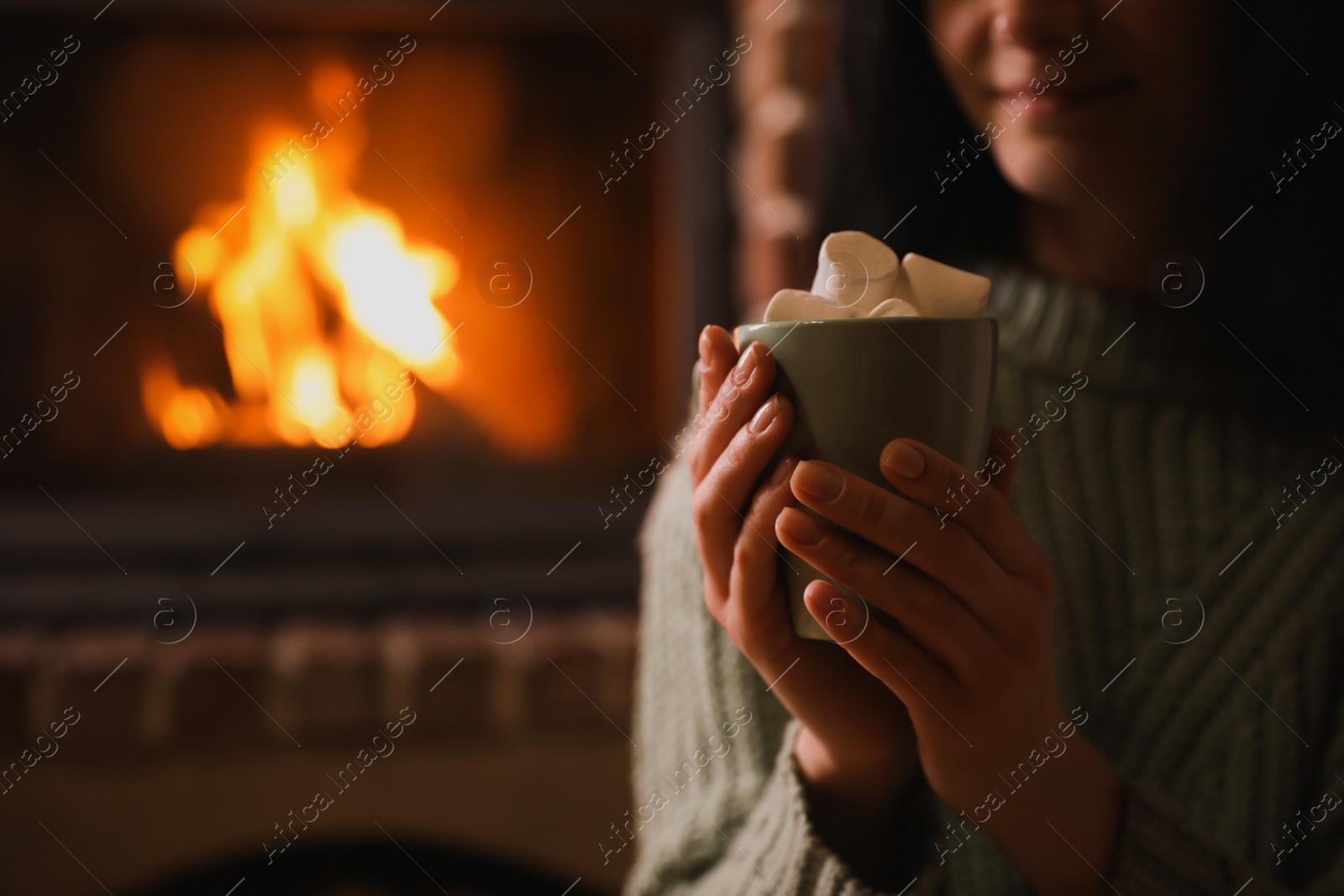 Photo of Woman with cup of sweet cocoa near fireplace indoors, closeup