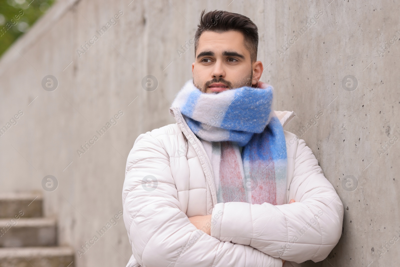 Photo of Handsome man in warm scarf near wall outdoors. Space for text