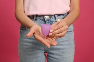 Photo of Young woman with menstrual cup on bright pink background, closeup