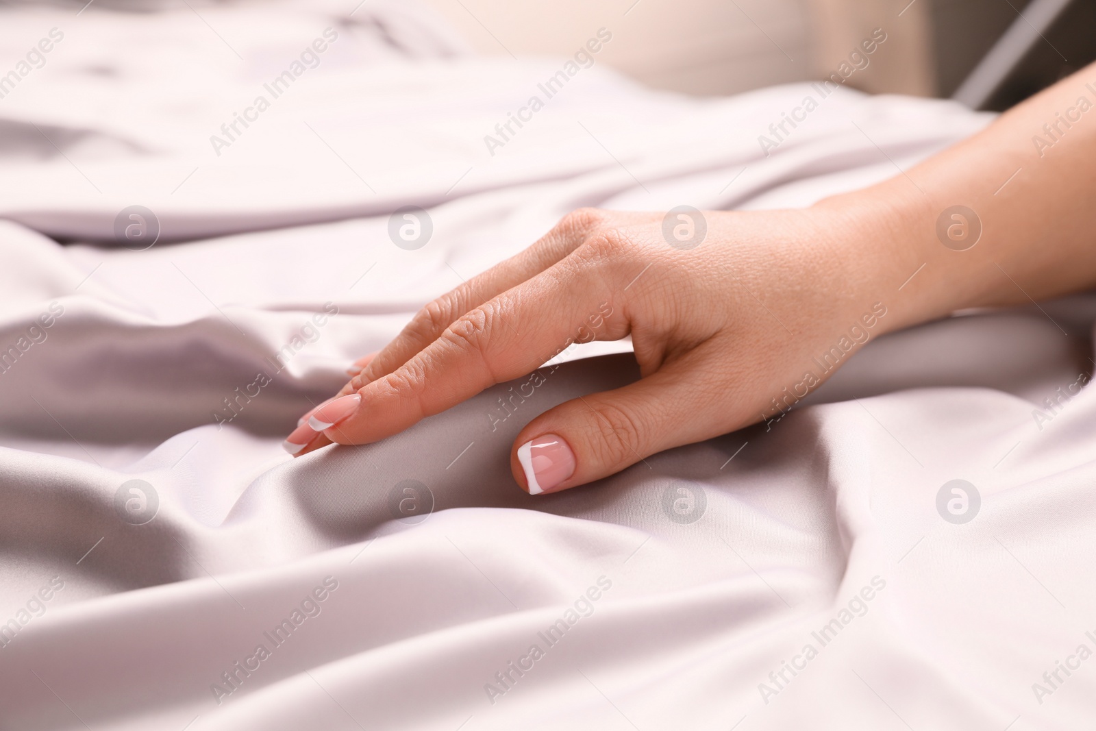 Photo of Woman touching smooth silky fabric indoors, closeup