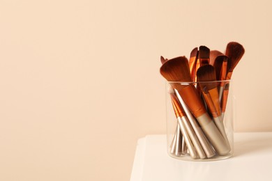 Photo of Set of professional makeup brushes on white table against beige background. Space for text