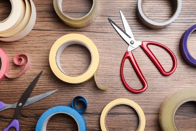 Photo of Rolls of adhesive tape and scissors on wooden background, flat lay