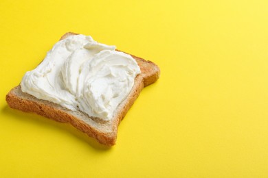 Photo of Slice of bread with tasty cream cheese on yellow background, space for text