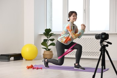Photo of Happy sports blogger training with resistance band while recording fitness lesson at home