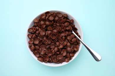 Breakfast cereal. Chocolate corn flakes in bowl and spoon on light blue table, top view