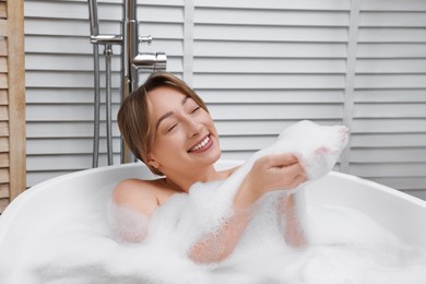 Photo of Happy woman taking bath with foam in tub indoors