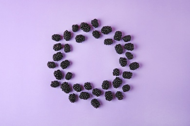 Photo of Frame made of tasty blackberries on purple background, top view with space for text