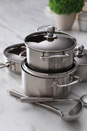 Photo of Set of new clean cookware and kitchen utensils on white marble table