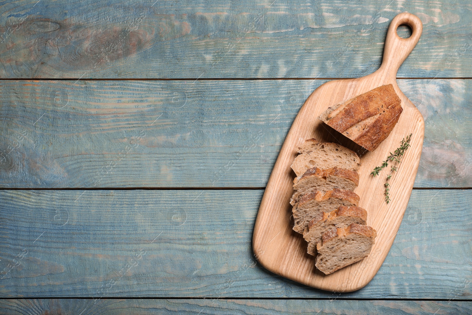 Photo of Cut buckwheat baguette with thyme on light blue wooden table, top view. Space for text