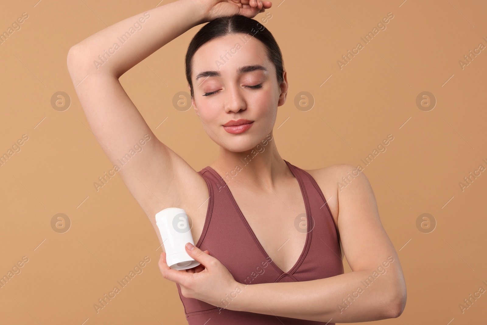 Photo of Beautiful woman applying deodorant on beige background