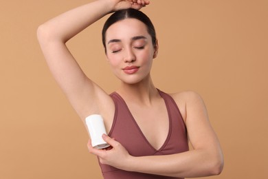 Beautiful woman applying deodorant on beige background