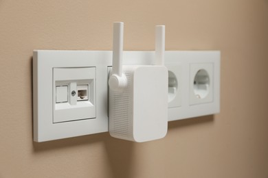 Photo of Wireless Wi-Fi repeater in power socket on beige wall