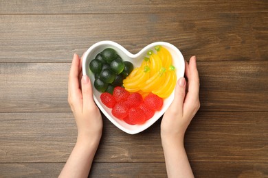 Photo of Woman with delicious gummy candies at wooden table, top view