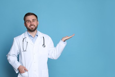 Photo of Portrait of young doctor showing something on light blue background. Space for text