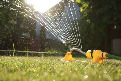 Photo of Automatic sprinkler watering green grass on sunny day in garden. Irrigation system