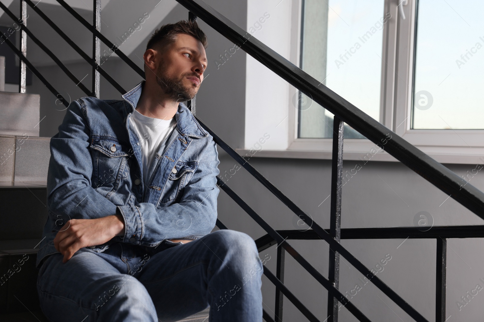 Photo of Upset man sitting on stairs indoors, space for text. Loneliness concept