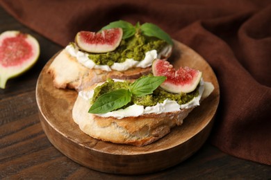 Tasty bruschettas with cream cheese, pesto sauce, figs and fresh basil served on wooden table, closeup