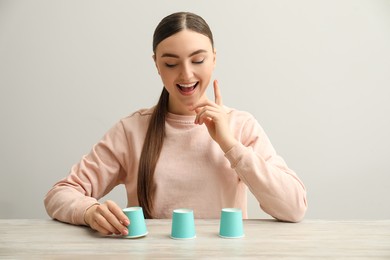 Photo of Shell game. Happy woman showing ball under cup at wooden table